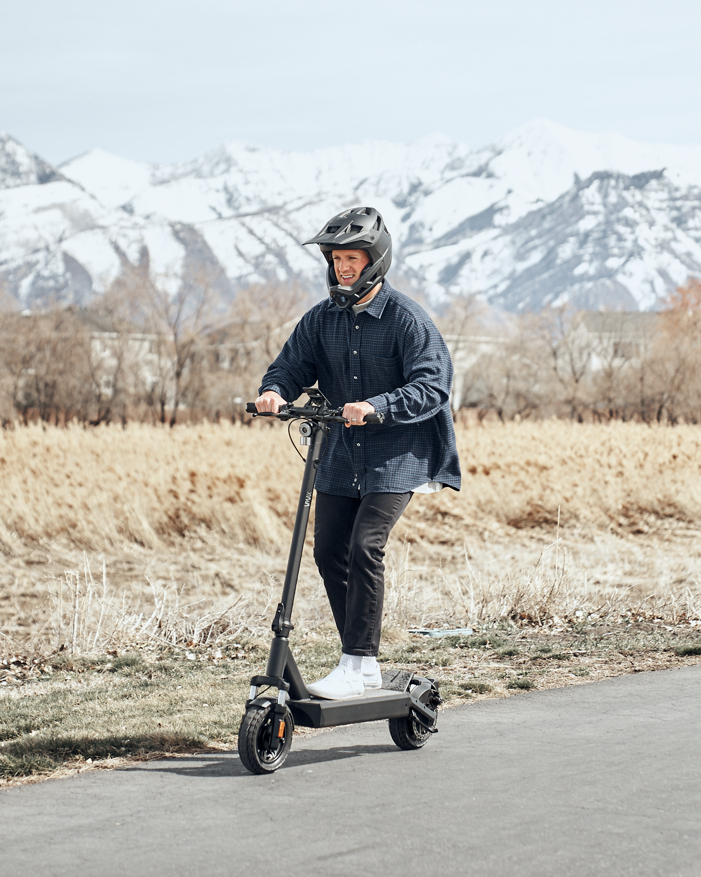 Ein Mann auf einem VMAX E-Scooter fährt auf der Strasse, im Hintergrund sind Berge zu sehen.